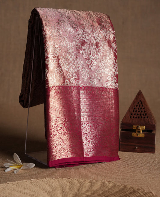 Pastel maroon Colour Kancheepuram tissue silk saree adorned with intricate silver floral zari work on the body, beautifully highlighted by a maroon traditional Rudraksham and floral design border, and paired with a matching blouse.