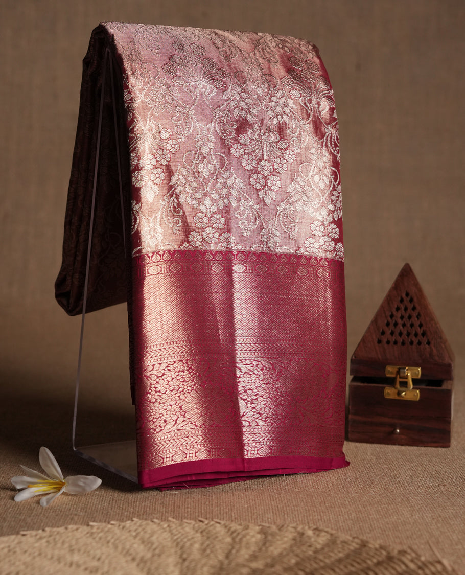 Pastel maroon Colour Kancheepuram tissue silk saree adorned with intricate silver floral zari work on the body, beautifully highlighted by a maroon traditional Rudraksham and floral design border, and paired with a matching blouse.