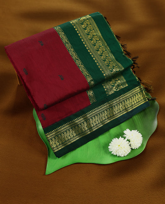Maroon colour mixed Kalyani cotton saree featuring Green zari motifs throughout the body, paired with a Green colour traditional border and pallu, with matching blouse