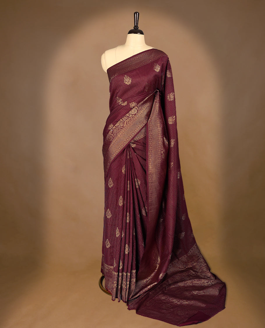 Maroon coloured semi Banaras georgette saree featuring golden Zari checks with floral motifs on the body, complemented by a self coloured traditional border with floral kodi design and a matching blouse.