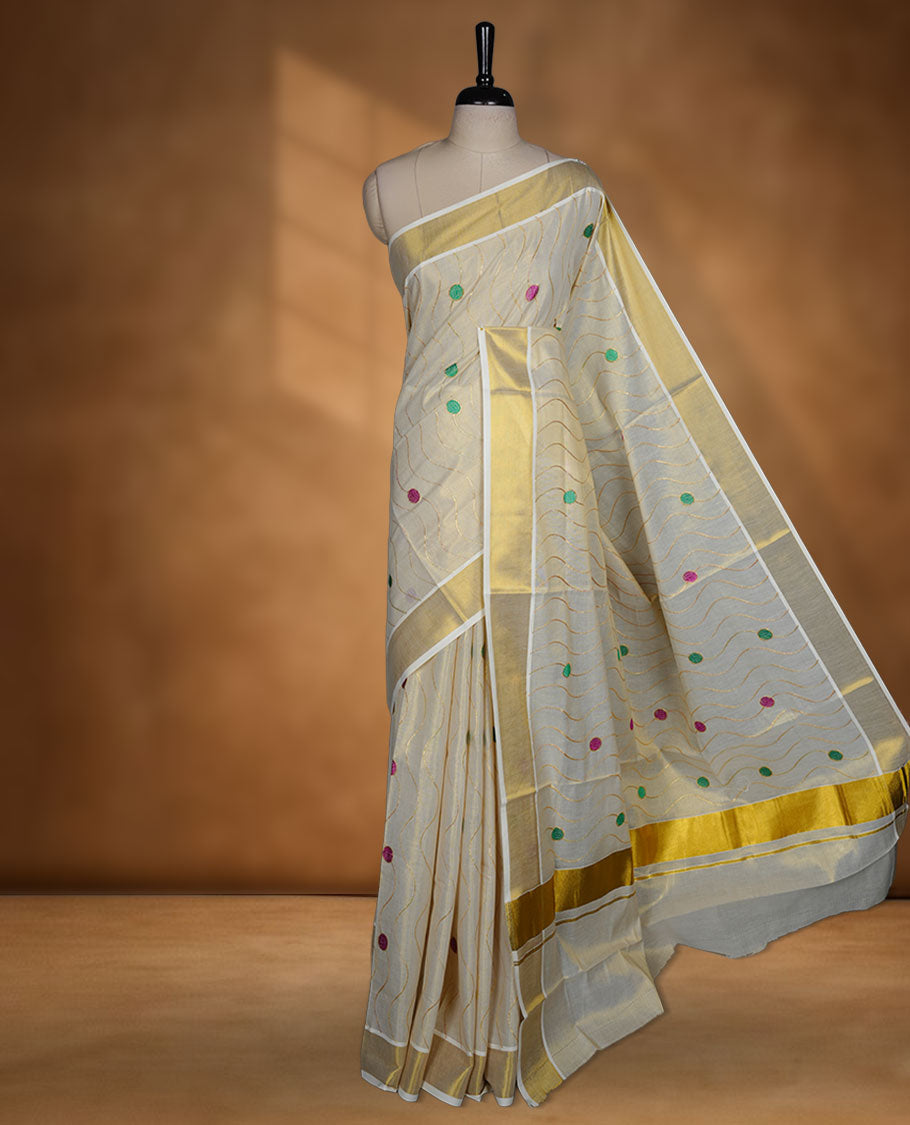 Off white colour cotton Kerala saree with wavy zari lines and colourful motifs, complemented by a classic golden zari border and matching blouse.
