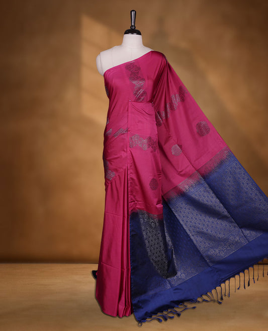 Magneta colour semi soft silk saree adorned with delicate woven floral motifs on the body, complemented by a contrast blue colour woven pallu with intricate detailing and tassel accents without border & Comes with a matching blouse piece.