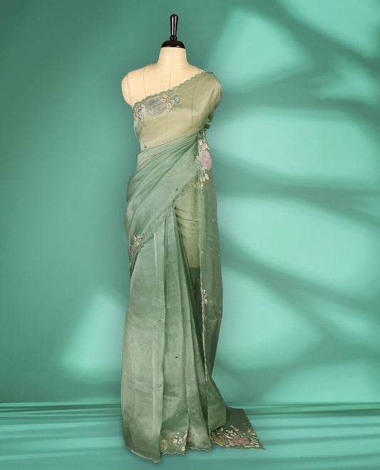 Pastel Green Colour organza saree featuring delicate floral embroidery with applique, bead, mirror, and thread detailing on the body and scalloped border, lending a soft feminine charm, paired with a matching blouse.