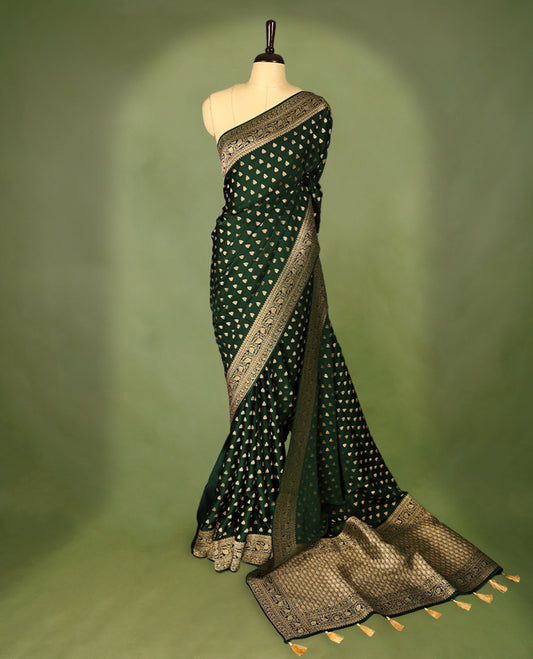 Bottle green semi-Banaras satin crepe saree featuring traditional closely woven buttas on the body, complemented by an antique-style border and a matching self-coloured blouse.