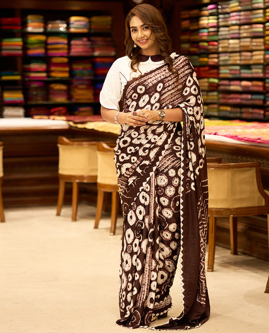 Medium coffee brown colour modal satin crepe saree featuring intricate hand done Shibori and Bandhej designs, enhanced by its smooth texture and paired with a matching blouse.