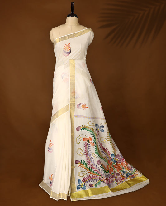 Elegant off white colour cotton Kerala saree with multicolor hand painted floral motifs on the pallu, scattered buttas on the body, and a golden zari border, blending traditional charm with artistic elegance.