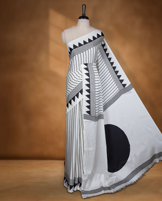 White colour semi modal saree highlighted with black triangle border accents and sleek striped detailing across the drape, featuring a bold oversized black circular motif on the pallu, paired with a matching printed blouse.