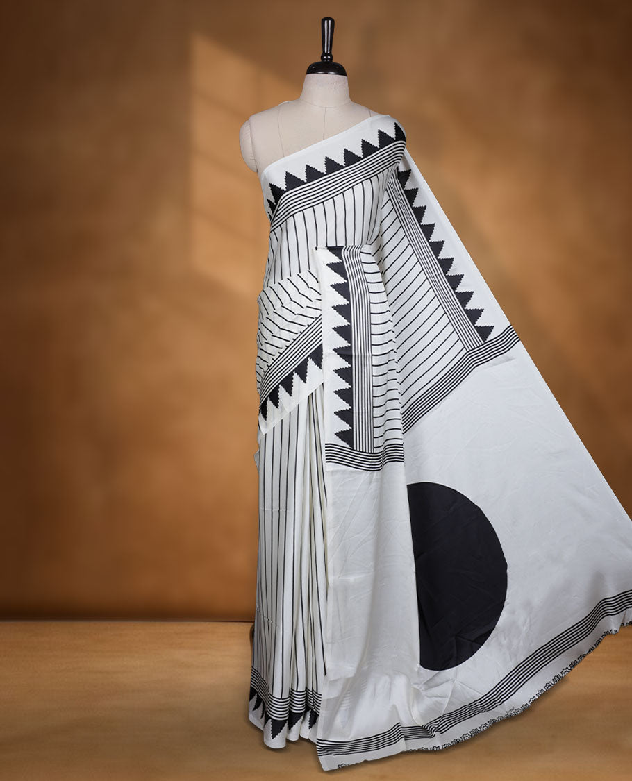 White colour semi modal saree highlighted with black triangle border accents and sleek striped detailing across the drape, featuring a bold oversized black circular motif on the pallu, paired with a matching printed blouse.