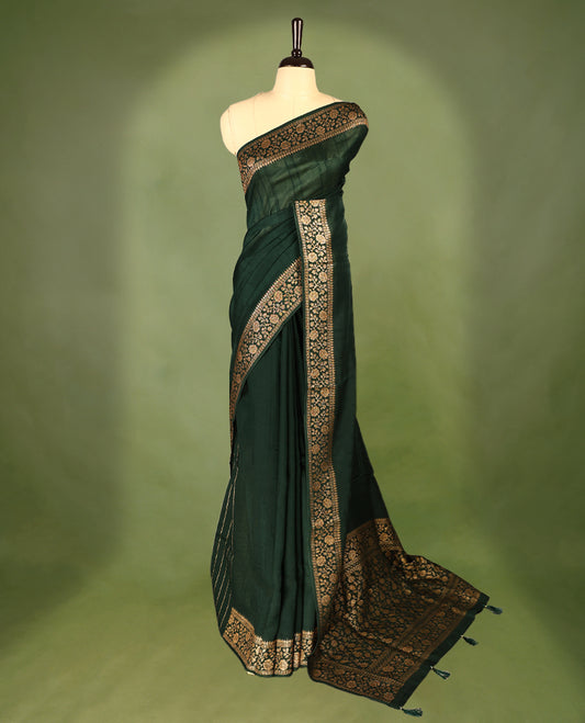 Bottle Green colour Tussar Banaras saree featuring a plain body, rich floral woven zari border and grand pallu, paired with a matching blouse for an elegant and regal traditional look.