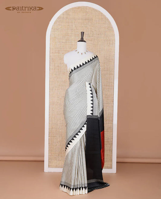 White semi modal crepe saree adorned with black vertical line prints, highlighted by a temple border and circle butta design on the pallu, paired with a coordinated printed blouse.