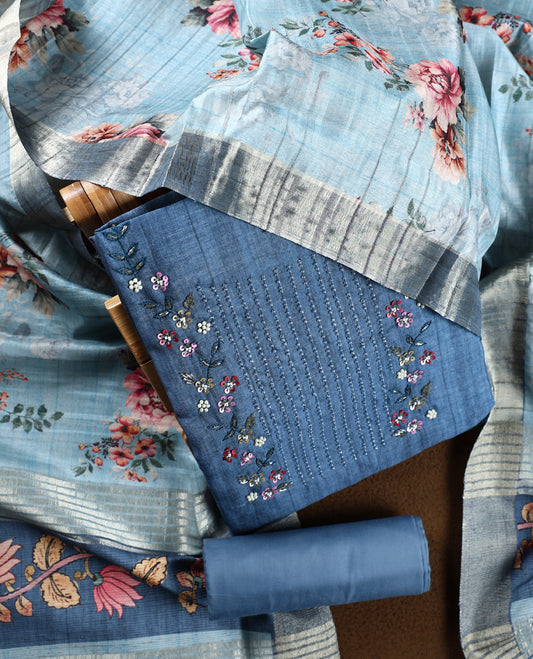 Dark pastel blue colour churidhar material adorned with floral embroidery and sewn glass beads on the yoke, paired with a plain blue bottom and a beige dupatta featuring floral prints.