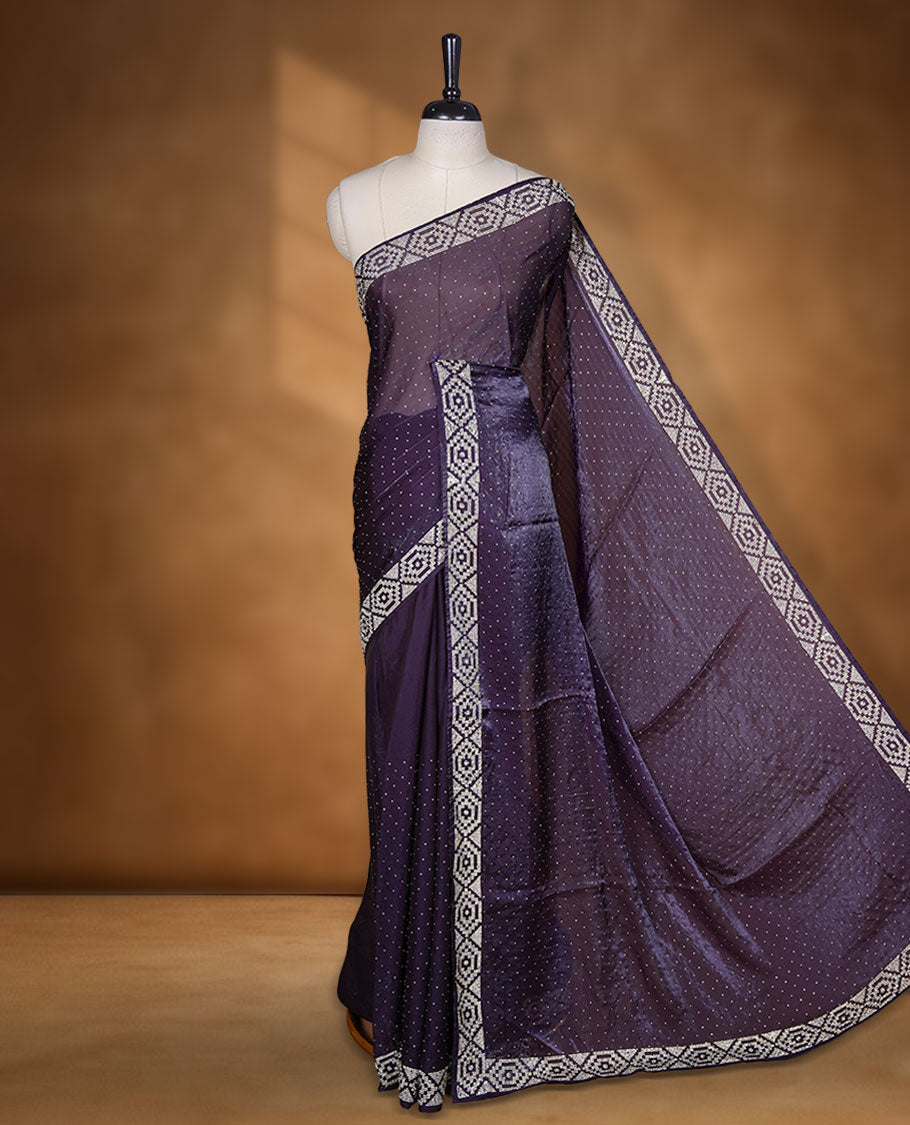 Dark purple colour chiffon designer saree, featuring delicate scattered stone detailing all over the body, highlighted with intricate stone work and a heavy geometric stone pattern along the border and pallu, paired with a matching embellished blouse.