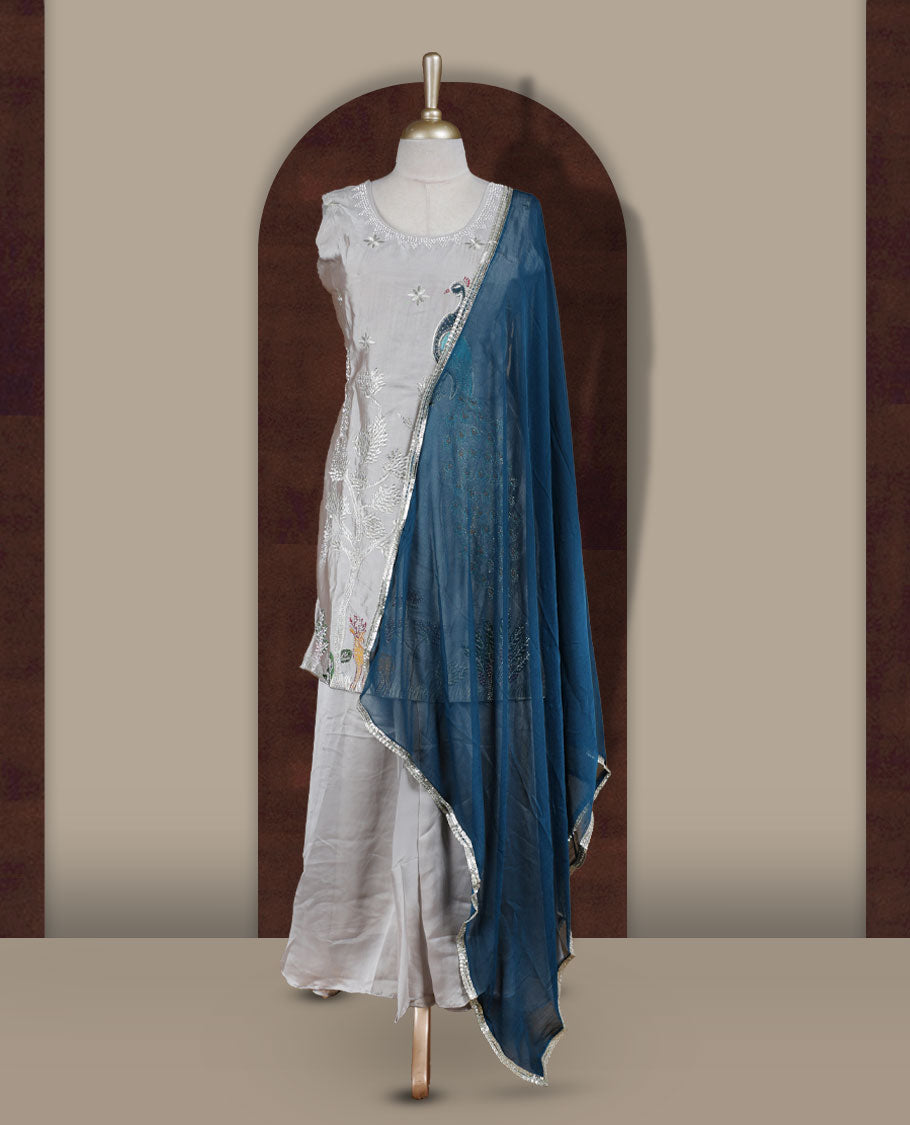 Elegant Ice grey colour embroidered sharara set featuring intricate peacock motifs and delicate stone detailing & Paired with a rich teal blue dupatta edged in silver and flared bottom.