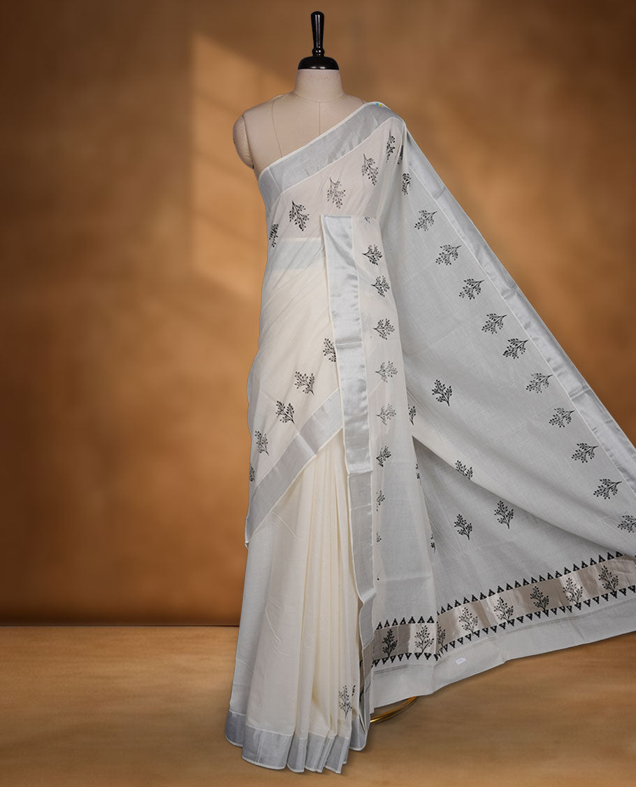 Off-white colour cotton Kerala saree featuring a subtle silver-toned border, adorned with delicate black leafy motifs across the body and pallu, and paired with a matching blouse.