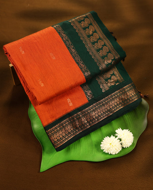 Rust Orange colour mixed Kalyani cotton saree featuring Copper zari motifs throughout the body, paired with Bottle Green colour traditional border and pallu, with matching blouse