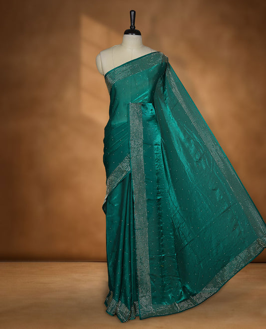 Emerald green chiffon designer saree, featuring dainty scattered stones on the body, enriched with dense stone work and a heavy metallic stone border and pallu, paired with a matching blouse.