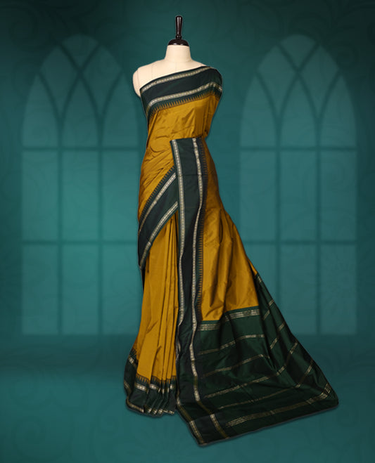 Mustard semi silk saree with plain body, vibrant deep green pallu and matching green border adorned with golden zari, accented with temple motifs along the edges, Paired with a matching blouse, perfect for festive occasions.