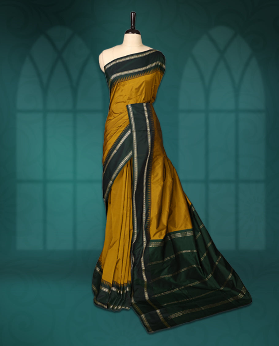 Mustard semi silk saree with plain body, vibrant deep green pallu and matching green border adorned with golden zari, accented with temple motifs along the edges, Paired with a matching blouse, perfect for festive occasions.