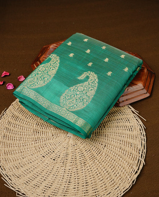 Green colour semi tussar silk saree featuring small gold zari mango motifs across the body, enhanced with a self colour border showcasing elegant gold zari mango patterns. Paired with a matching blouse piece.