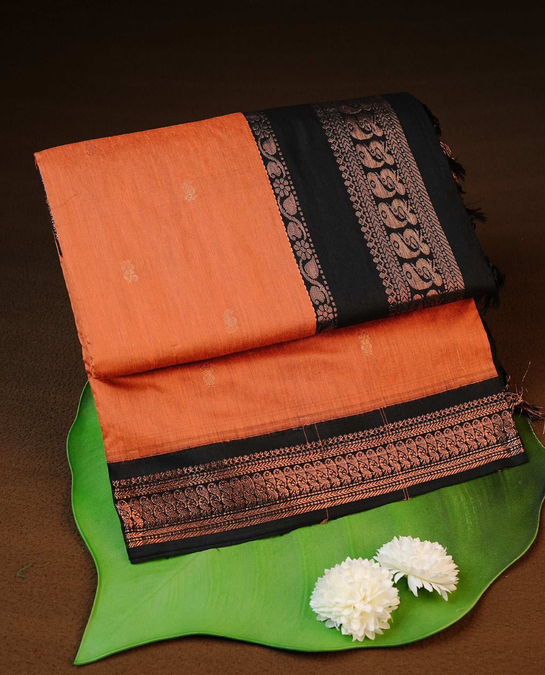 Orange colour kalyani cotton saree featuring antique zari motifs on body, complemented by Black colour with Antique zari border, paired with matching blouse piece.