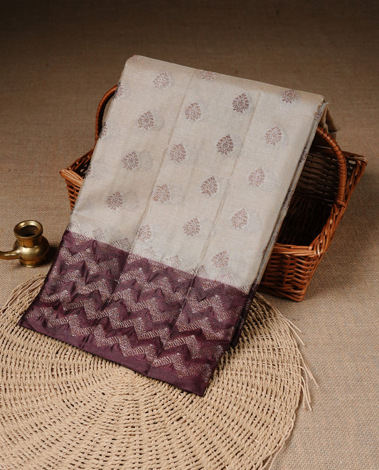 Cream Colour Tussar silk saree featuring Antique Zari motifs on body, Finished with contrast Chocolate colour Zigzag zari pattern border, paired with matching blouse piece.