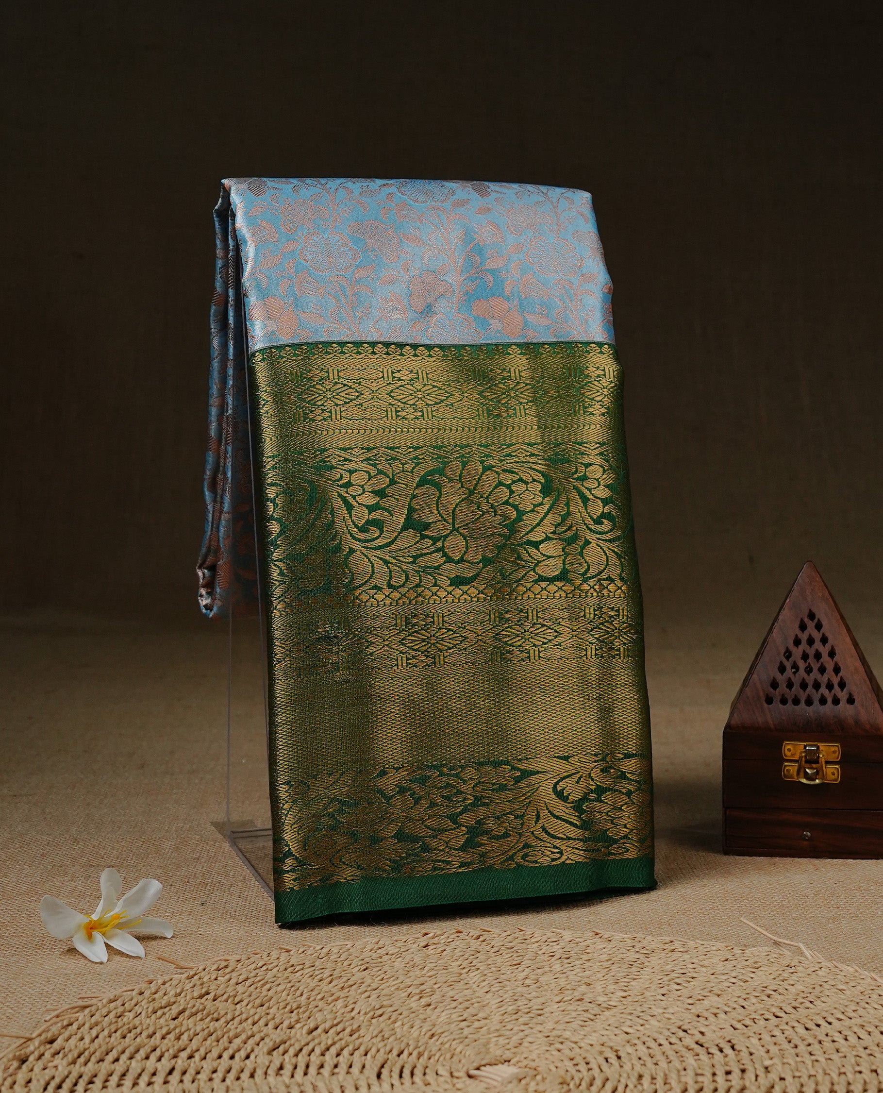 Ice Blue Colour Tissue saree Featuring Light gold Floral kodi Pattern on body, enhanced with contrast Green colour with gold zari border, paired with matching blouse piece.