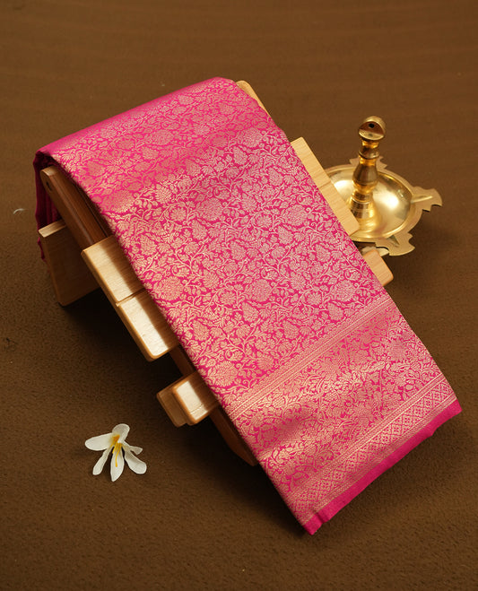 Rani pink colour semi silk brocade saree featuring intricate Gold Floral kodi patterns across the body, complemented by a rich self colour woven border and pallu, paired with a matching blouse.