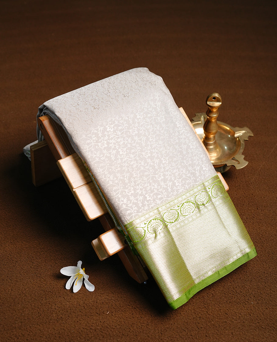 Silver colour semi wedding saree featuring silver zari floral kodi pattern on body, contrast Light green colour with traditional border, paired with matching blouse piece.