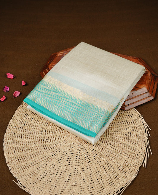 White cream colour Semi Tussar silk saree featuring an elegant plain body, accentuated by a contrast Aqua border adorned with intricate gold zigzag zari work, paired with a matching blouse piece.