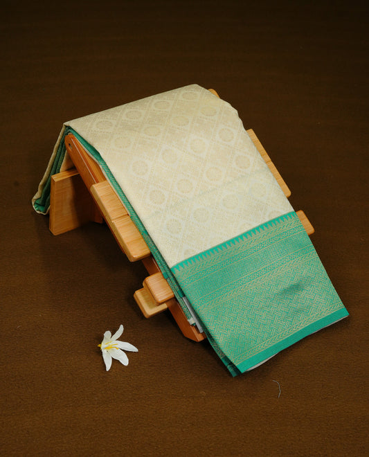 Cream Colour Semi Soft Silk Saree Featuring Gold zari Box With motifs Pattern On Body, Highlighted  by contrast Green border with Gold zari, paired with matching blouse piece.