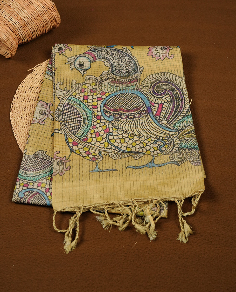 Mustard yellow colour semi tussar silk saree with Kalamkari-inspired peacock pallu, floral printed body, subtle textured weave, and tassel finish, paired with a matching printed blouse piece.