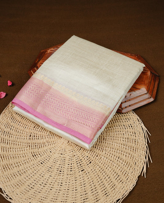 White cream colour Semi Tussar silk saree featuring an elegant plain body, accentuated by a contrast Pink border adorned with intricate gold zigzag zari work, paired with a matching blouse piece.