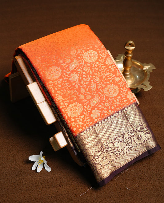 Orange colour semi wedding saree featuring gold zari floral kode pattern on body, contrast chococlate colour with traditional border, paired with matching blouse piece.