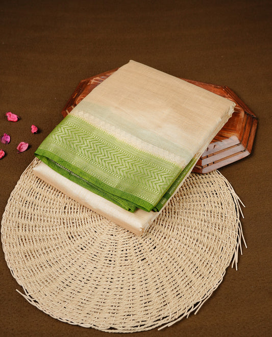 Cream colour Semi Tussar silk saree featuring an elegant plain body, accentuated by a contrast olive border adorned with intricate gold zigzag zari work, paired with a matching blouse piece.