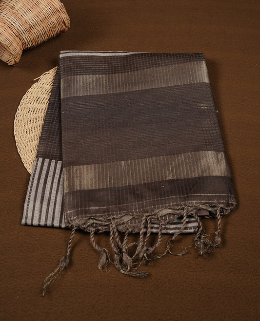 Charcoal Brown colour semi tussar silk saree crafted in breathable cotton, featuring subtle striped textures across the body, a minimalist pallu with fine linear detailing, and a coordinated plain blouse piece.