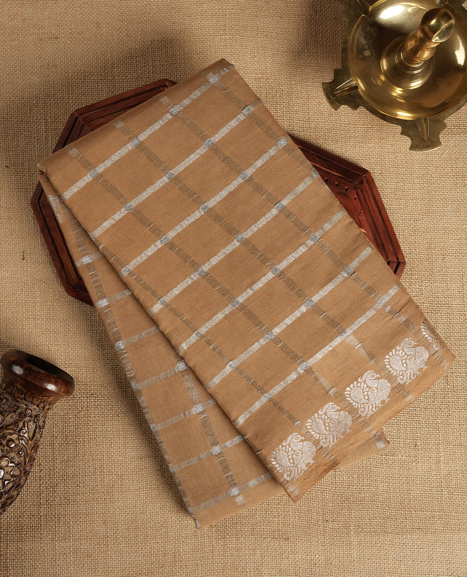Pastel brown colour Chettinad cotton saree featuring silver checked patterns on the body, accentuated with elegant silver peacock motifs along the border & Comes with a matching blouse piece.