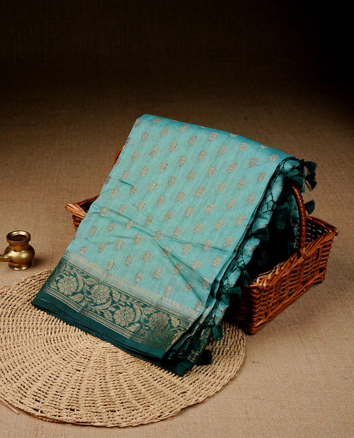 Sky blue colour Banaras silk saree featuring gold zari buttas on body, complemented by contrast teal colour border, comes with matching blouse piece.