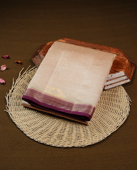 Cream colour Semi Tussar silk saree featuring an elegant plain body, accentuated by a contrast Purple border adorned with intricate gold zari work, paired with a matching blouse piece.