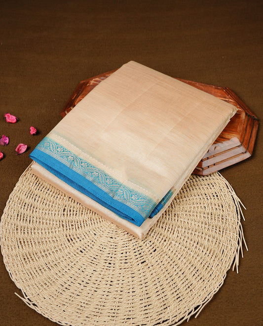 Cream colour Semi Tussar silk saree featuring an elegant plain body, accentuated by a contrast Blue border adorned with intricate gold floral kodi zari work, paired with a matching blouse piece.