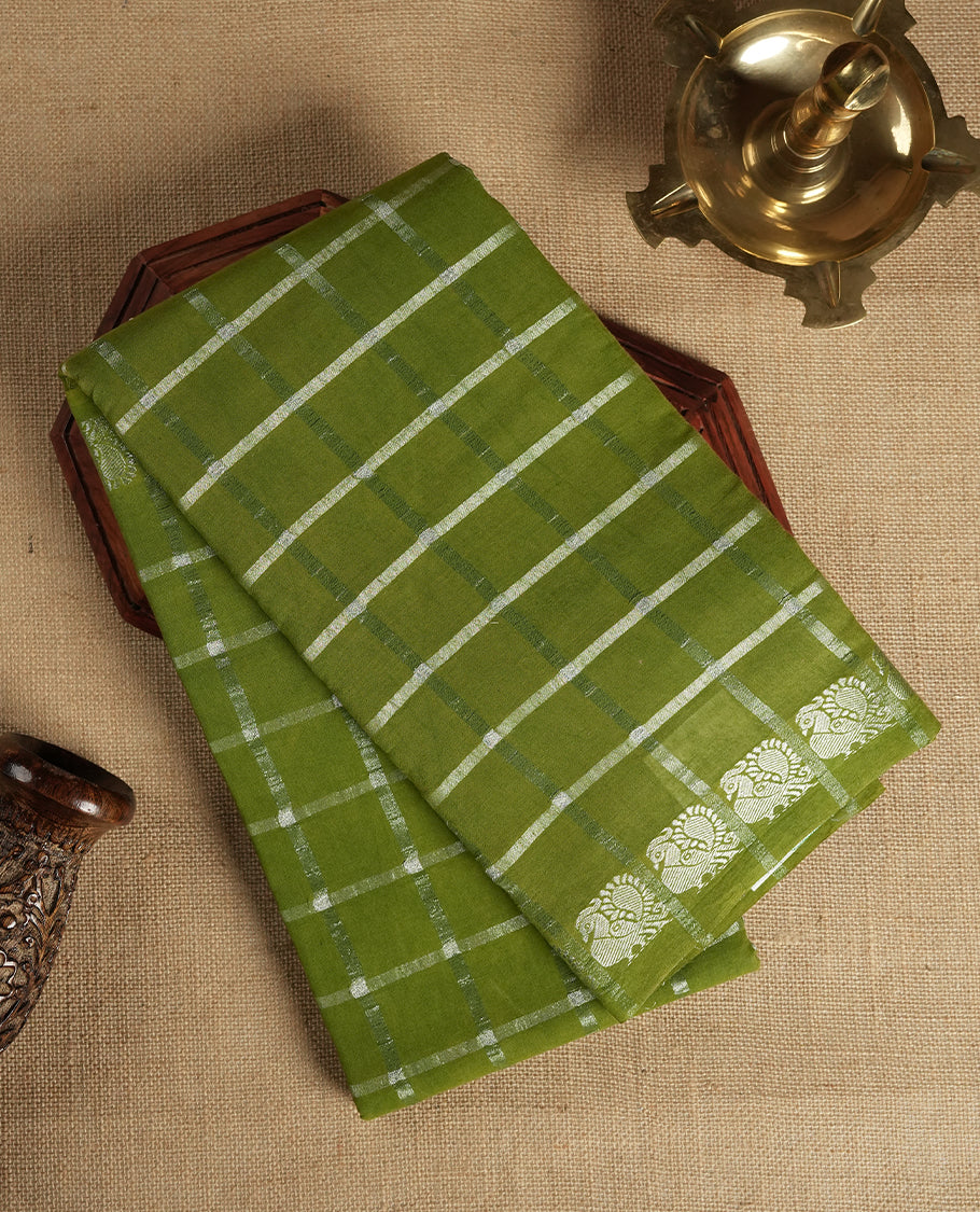 Olive green colour Chettinad cotton saree featuring silver checked patterns on the body, accentuated with elegant silver peacock motifs along the border & Comes with a matching blouse piece.
