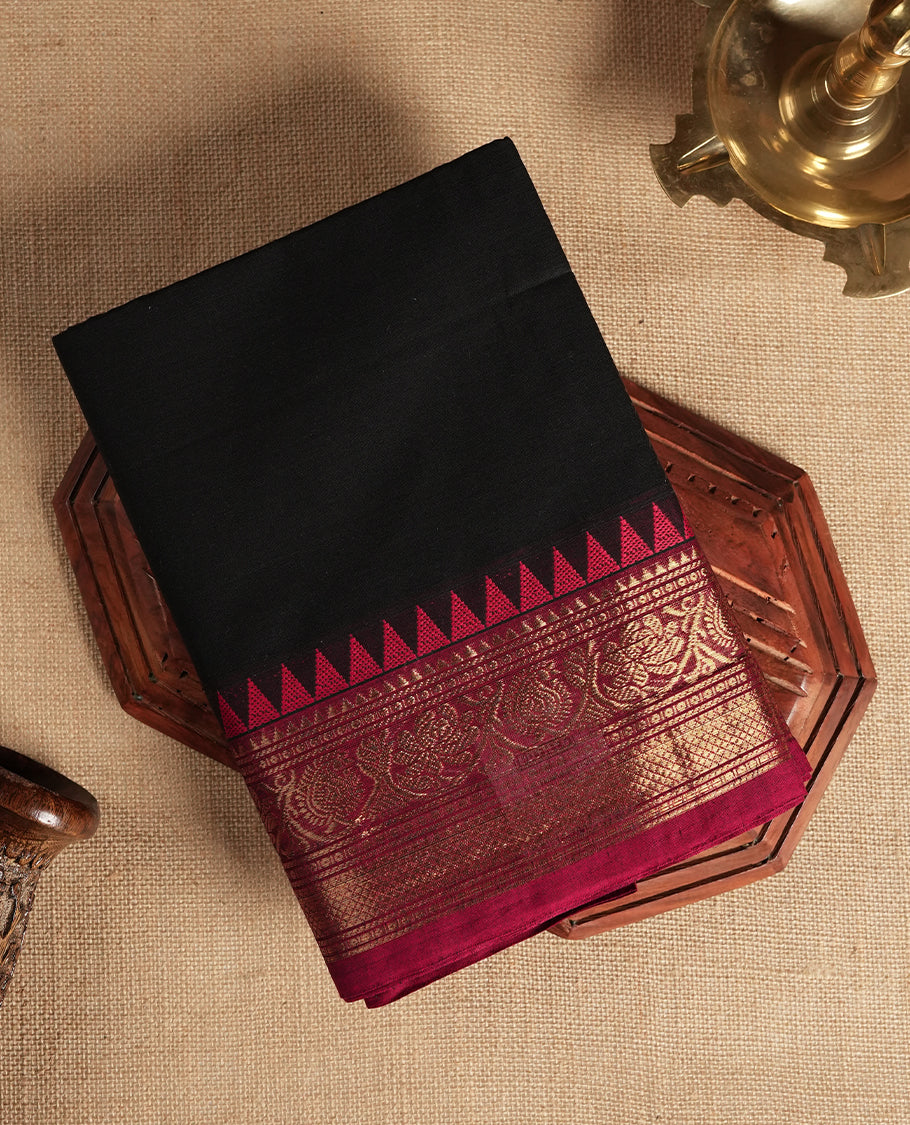 Black colour Chettinad cotton saree adorned with small woven motifs on the body, highlighted by a maroon border featuring intricate golden zari floral patterns and temple design & Comes with a matching blouse piece.