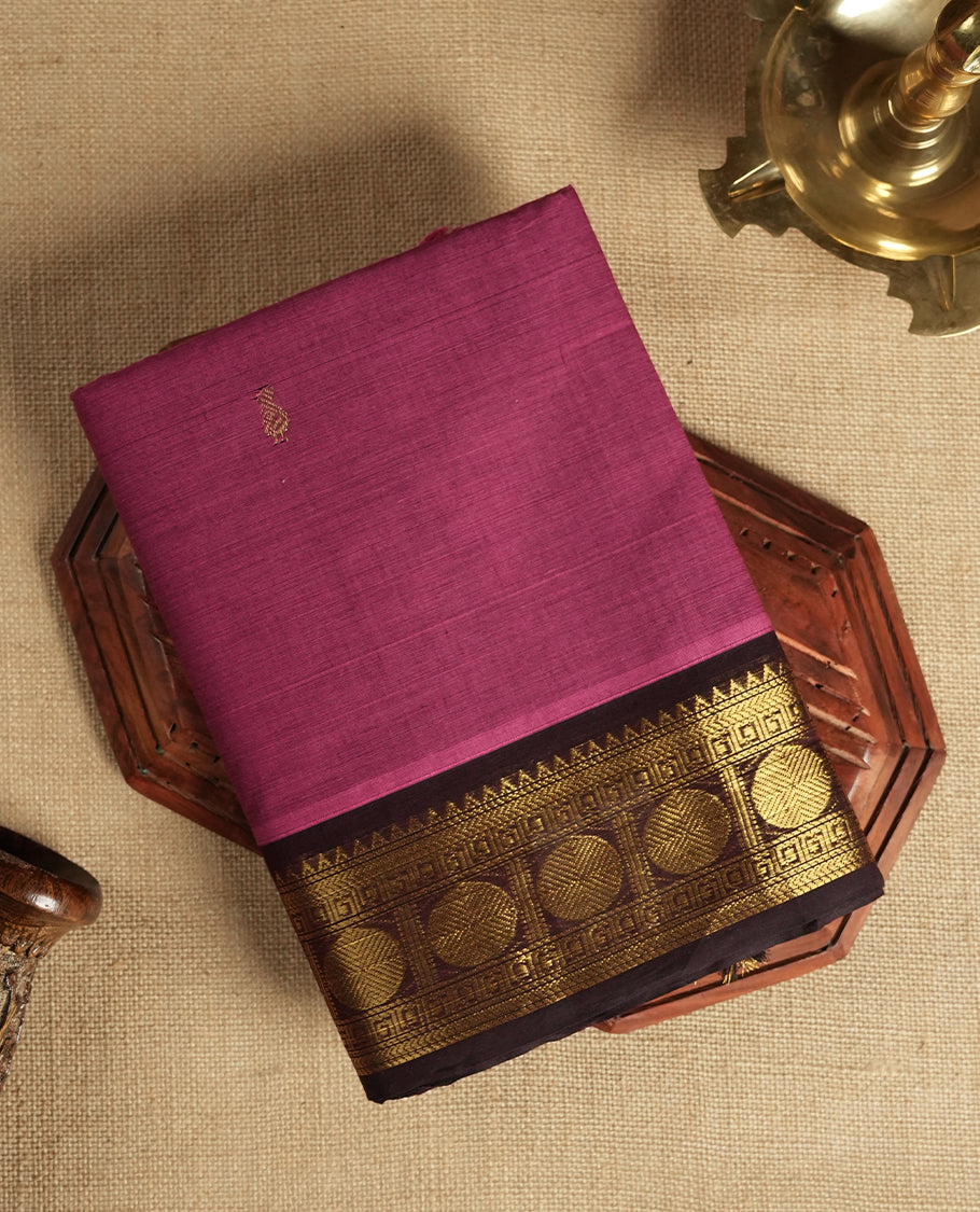 Magenta and Dark wine colour Chettinad cotton saree adorned with a single small woven motif on the body, highlighted by a golden zari border featuring circular patterns and intricate detailing & Paired with a matching blouse piece.