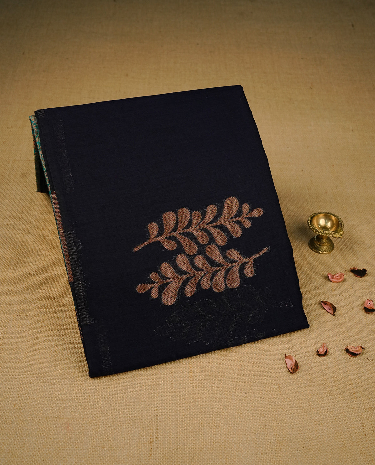 Navy blue colour semi linen saree with elegant gold zari leaf motifs across the body, complemented by a contrast peacock green pallu and a borderless design, paired with a matching blouse piece.