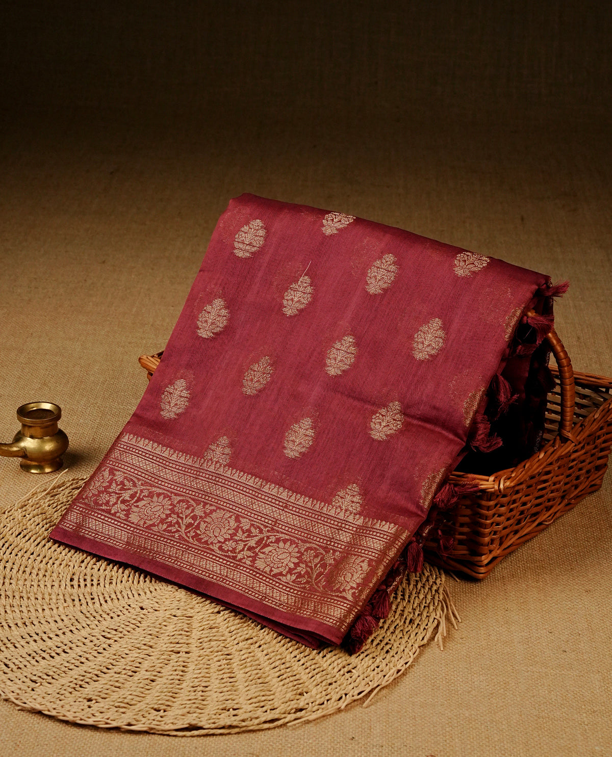 Maroon colour Banaras silk saree featuring gold zari buttas on body, complemented by self colour with zari border, comes with matching blouse piece.
