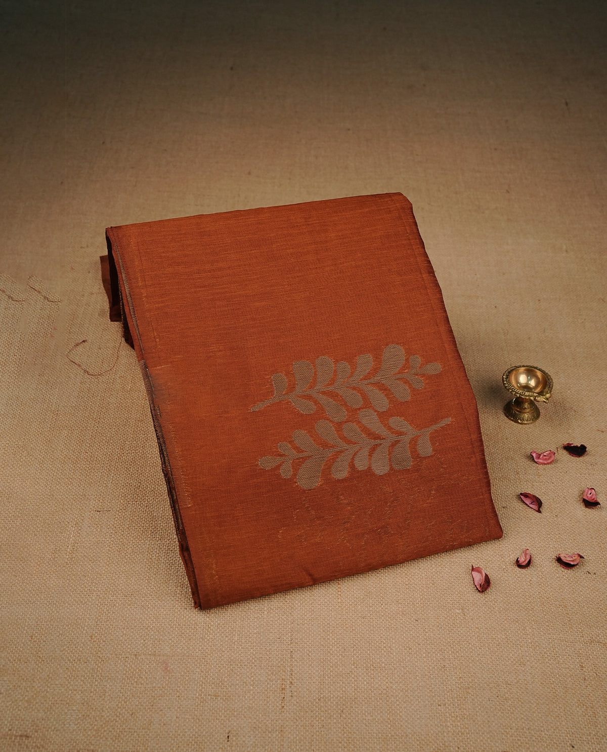 Rust orange colour semi linen saree with elegant gold zari leaf motifs across the body, complemented by a rich wine purple contrast pallu with intricate gold zari  works and a borderless design, paired with a matching blouse piece.