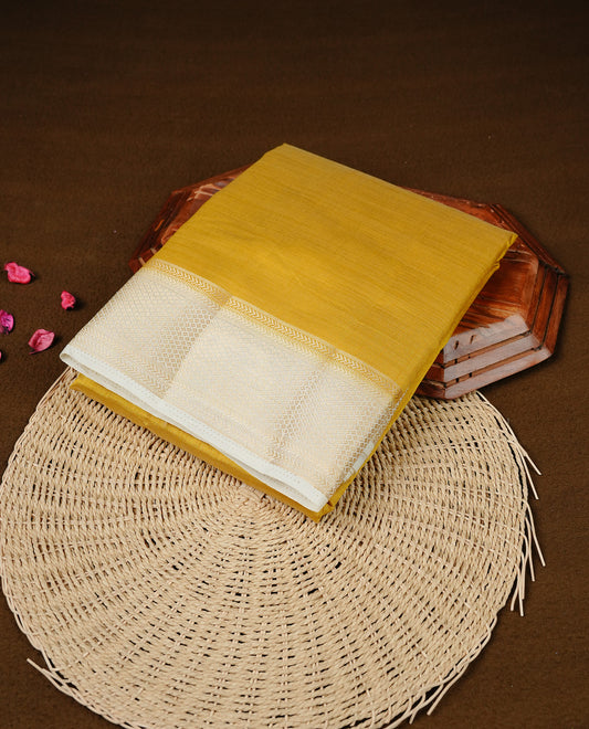 Mustard colour Semi Tussar silk saree featuring an elegant plain body, accentuated by a contrast cream border adorned with intricate gold zari work, paired with a matching blouse piece.