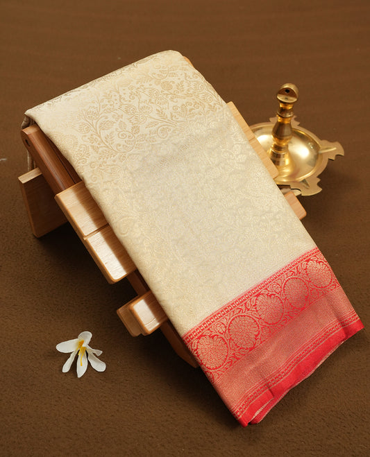 Cream colour semi silk brocade saree featuring intricate Gold floral kodi patterns across the body, complemented by a Contrast rich red colour woven border and pallu, paired with a matching blouse.