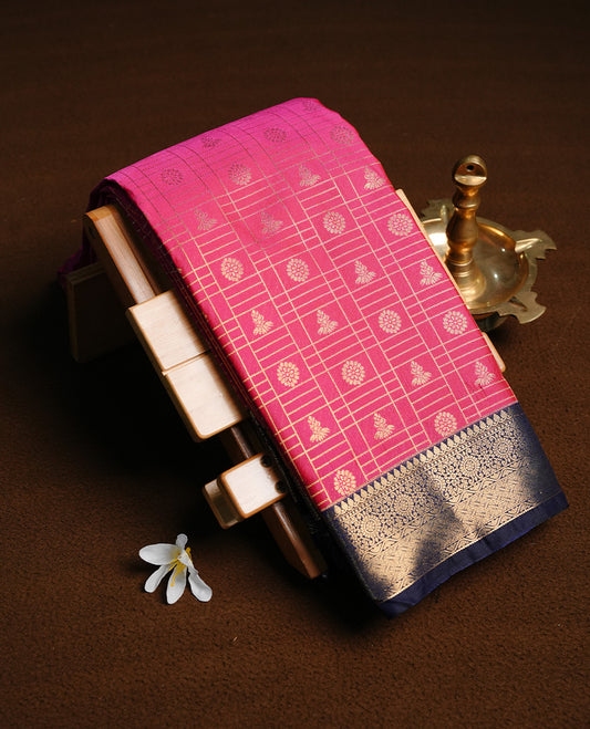 Magenta colour semi wedding saree featuring gold zari check with motifs on body, contrast Navy blue colour with traditional border, paired with matching blouse piece.