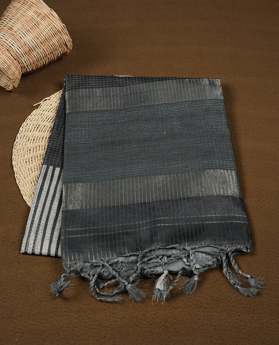 Soft charcoal grey colour semi tussar silk saree with fine striped texture and a subtle geometric body design. Finished with a classic striped pallu and tassel edges.