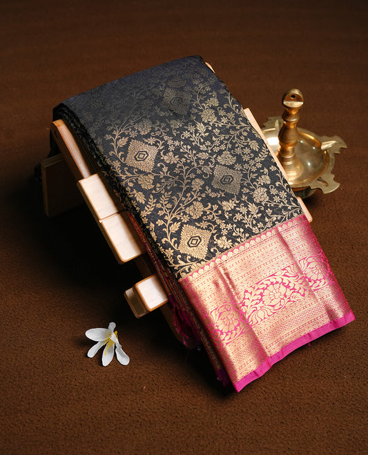Black colour semi wedding saree featuring gold zari floral kode pattern on body, complemented by contrast magenta with traditional border, paired with matching blouse piece.